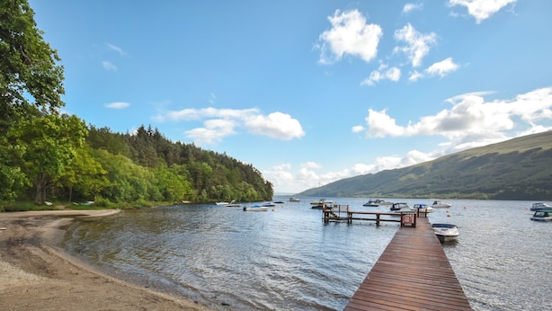 A wooden dock extending into a calm lake with boats anchored nearby. - 3 bedroom accommodation in Rowardennan (Rowardennan)