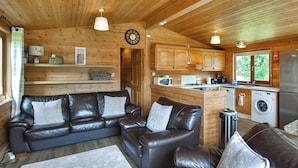 A cozy cabin interior with a leather sofa, a small dining table, wooden cabinets, and a kitchen area with a washing machine. - 3 bedroom accommodation in Rowardennan (Rowardennan)