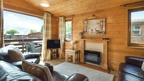 A wooden cabin interior with a leather sofa, a flat-screen TV, a fireplace, and a painting of deer. - 3 bedroom accommodation in Rowardennan (Rowardennan)