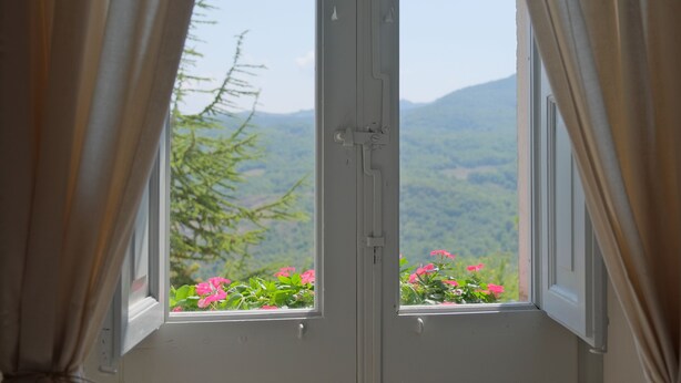 A window with curtains, a view of pink flowers, and a mountainous landscape. - La Dimora di Pindaro (Colledimacine)