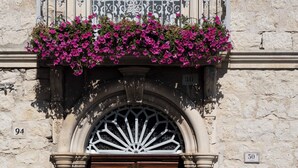 A double wooden door with a wrought iron gate, a stone wall, and a balcony with pink flowers. - La Dimora di Pindaro (Colledimacine)