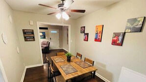 A dining area with a wooden table, chairs, and a ceiling fan. There are wall decorations and a door leading to another room. - Arlington House - 5 min to Arrowhead / FIFA (Independence)
