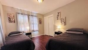 A bedroom with two beds, a window with curtains, a door, and wall art. - Arlington House - 5 min to Arrowhead / FIFA (Independence)