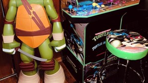 A life-sized Teenage Mutant Ninja Turtles arcade machine with a screen displaying a game, surrounded by a large Turtles figure and a stool. - Arlington House - 5 min to Arrowhead / FIFA (Independence)