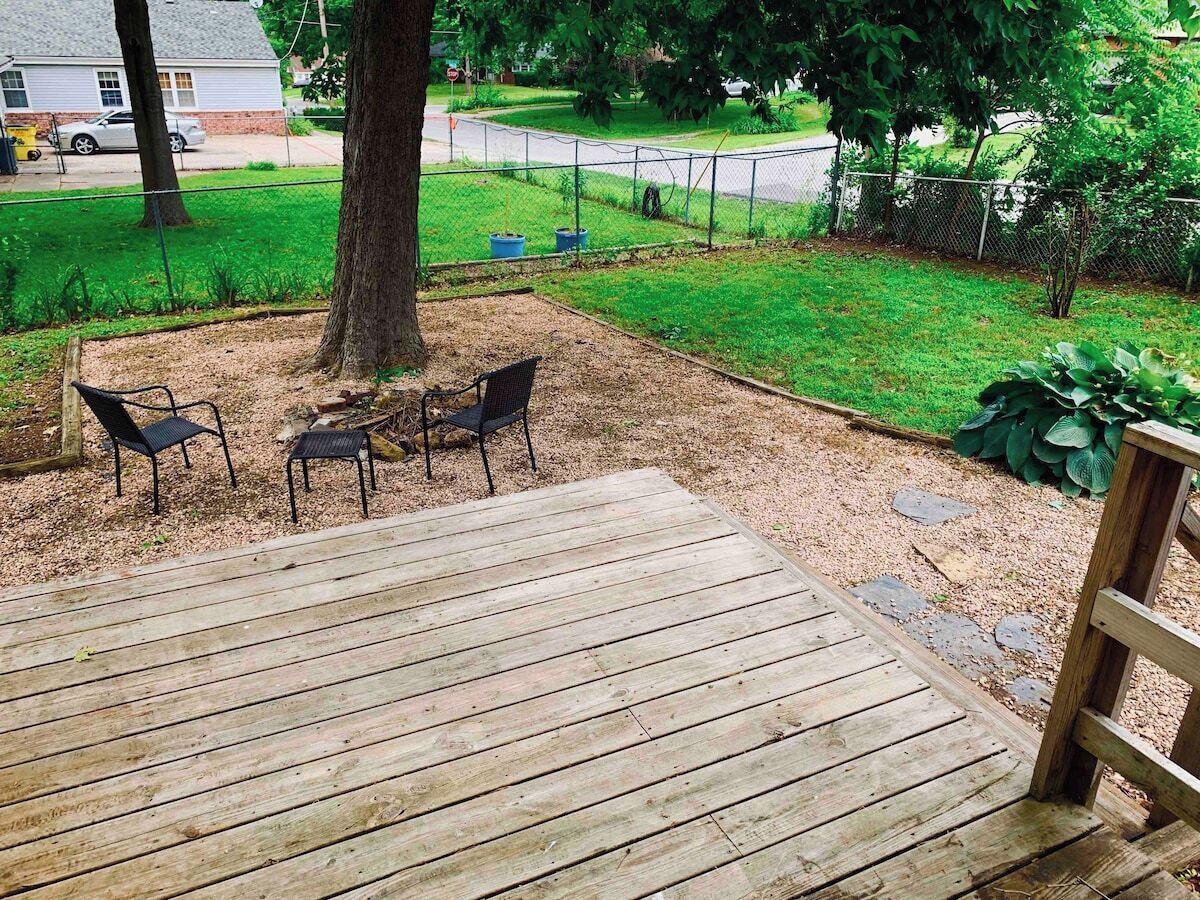 Een houten terras met drie stoelen en een boom op de achtergrond.