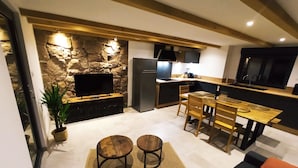 A modern kitchen with a stone accent wall, a dining area with a wooden table and chairs, and a cozy seating area with a sofa and ottoman. - Gîte des trois châteaux (Husseren-les-Châteaux)