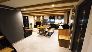 A modern kitchen with a stone accent wall, wooden dining table, and built-in appliances. - Gîte des trois châteaux (Husseren-les-Châteaux)