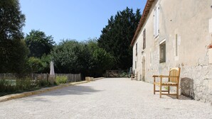 A gravel driveway leading to a rustic building with a wooden bench outside. - Gîtes au Château de Servanches, Dordogne, 20 Personnes, Piscine & Nature (Servanches)