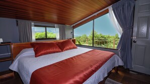 Un dormitorio con una cama grande, techo de madera y vistas a la vegetación por una ventana.