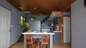 Una cocina con una isla central, sillas de madera y una escalera que sube a un nivel superior.