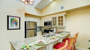 Una cocina con encimeras de granito, electrodomésticos de acero inoxidable y una barra desayunadora con sillas rojas.