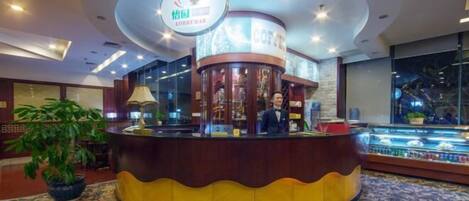 Un vestíbulo con una recepción, una cafetería y una planta grande en maceta.