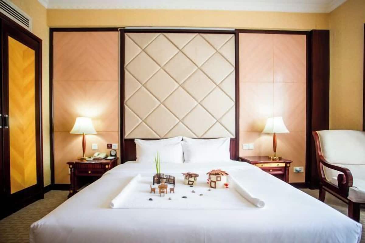 Una habitación de hotel con una cama grande, dos mesitas de noche, una silla y un cabecero decorativo.