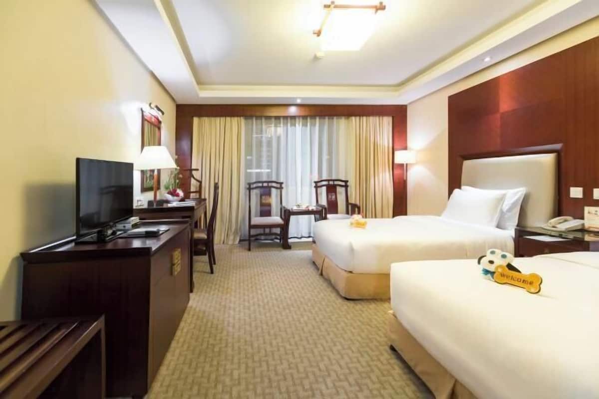Habitación de hotel con dos camas, un escritorio con televisor, una silla y una lámpara de escritorio.