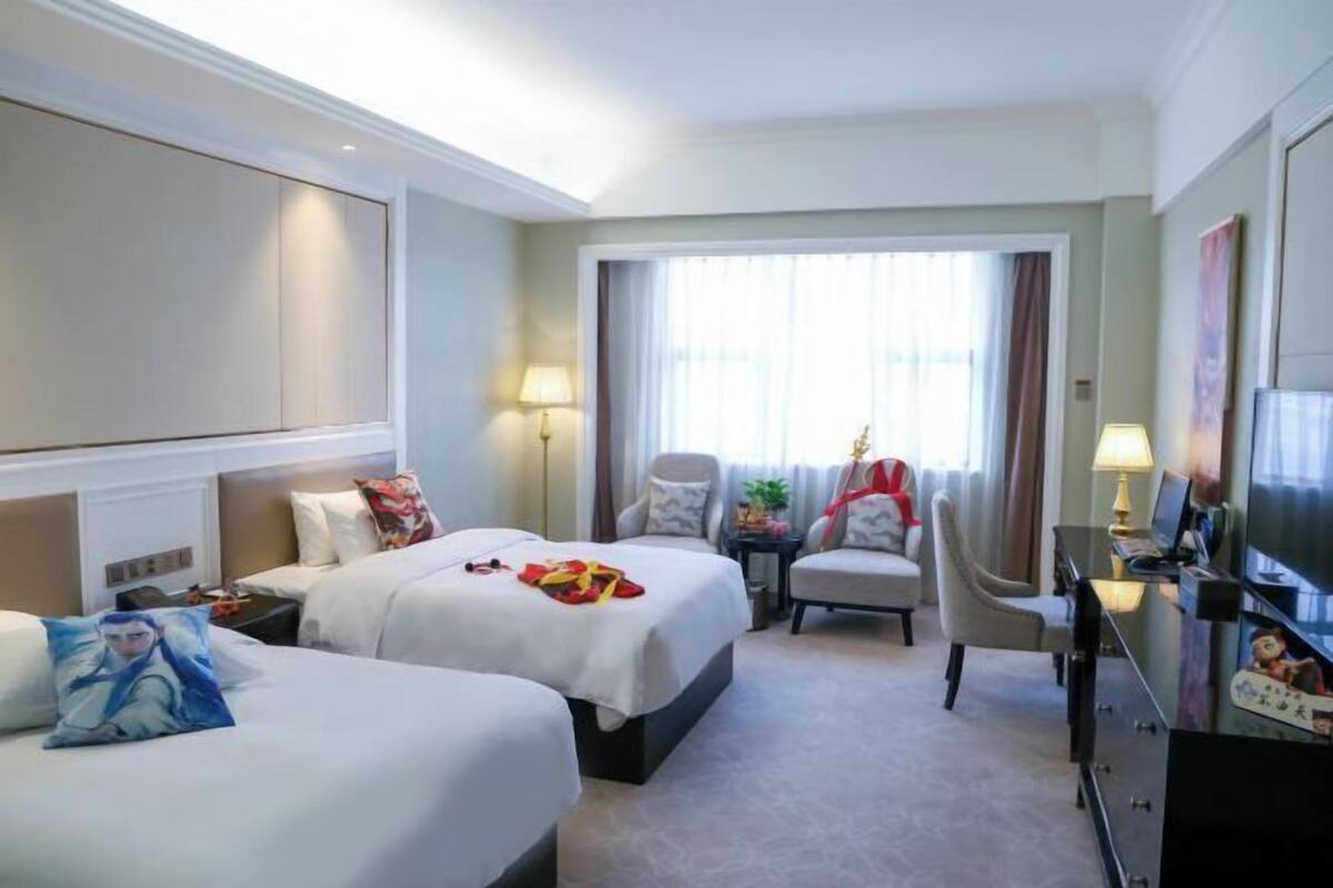 Habitación de hotel con dos camas, un escritorio, un televisor y una ventana con cortinas.