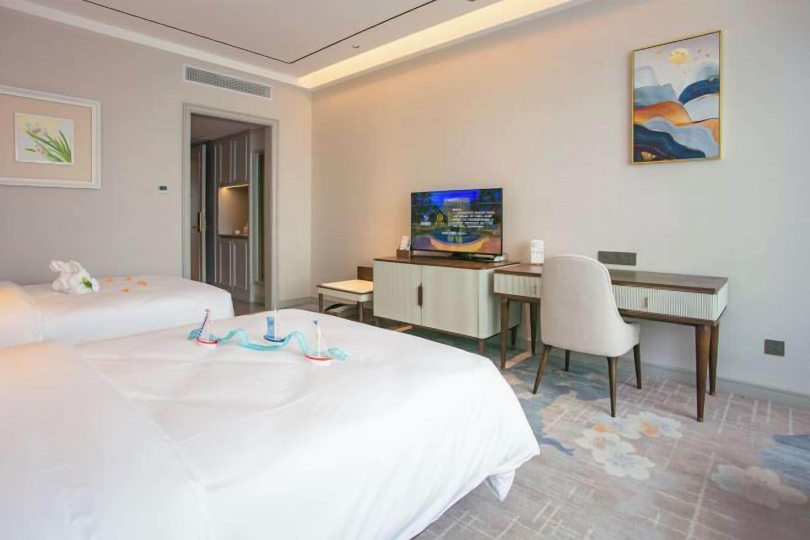 Een hotelkamer met twee bedden, een bureau, een televisietoestel en een schilderij aan de muur.
