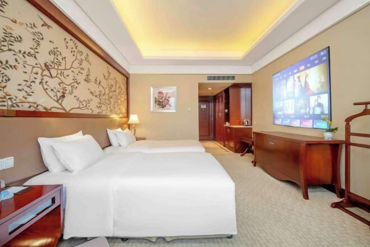 Habitación de hotel con dos camas, un escritorio, un armario, un televisor y un adorno en la pared.
