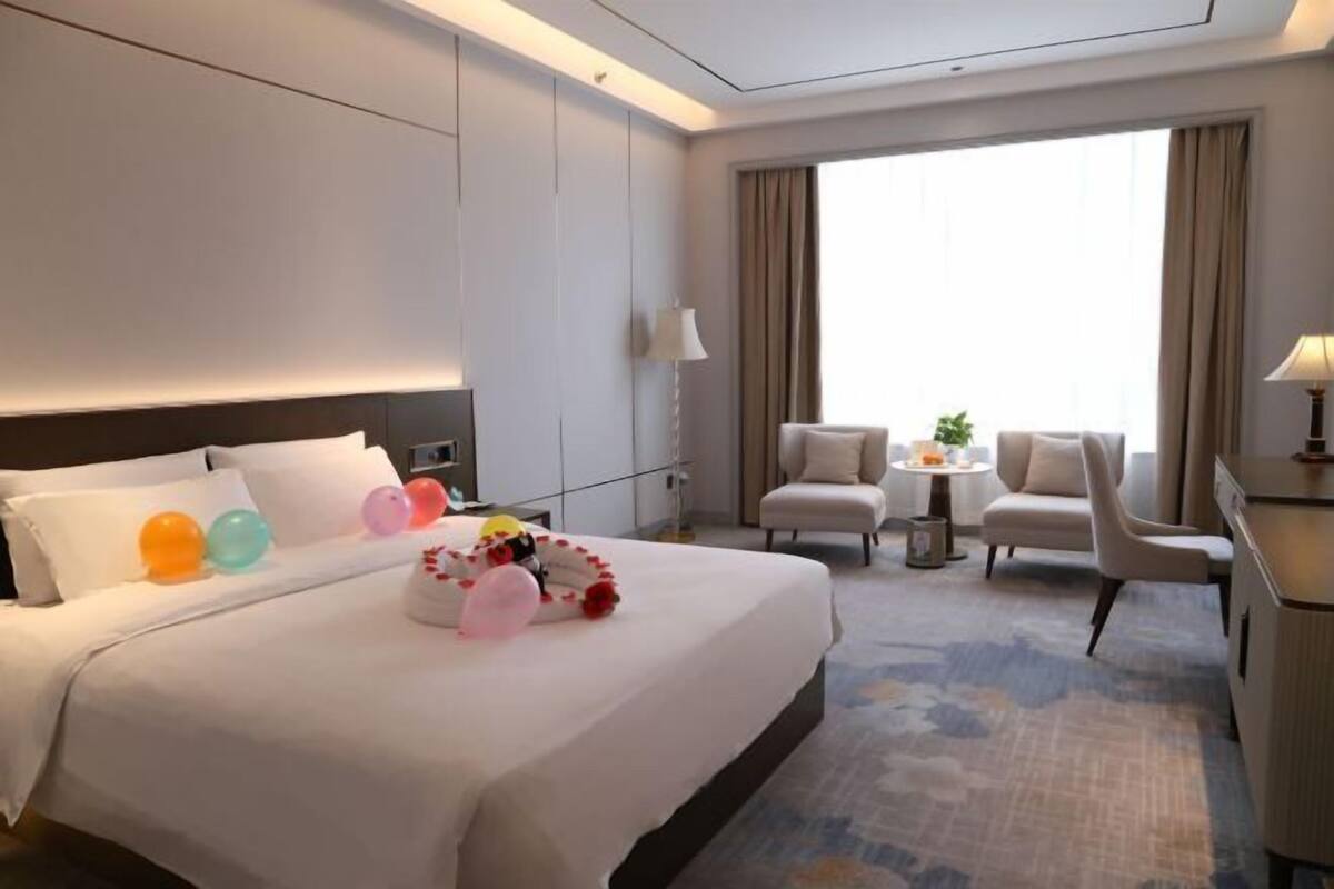 Habitación de hotel con una cama grande, dos sillones, una mesita y vistas al exterior a través de un ventanal.