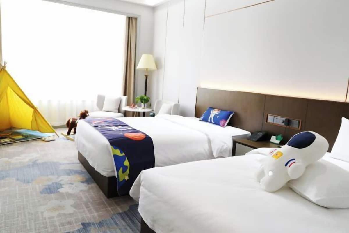 Habitación de hotel con dos camas, una tienda de campaña amarilla, una lámpara y un mullido juguete de astronauta.