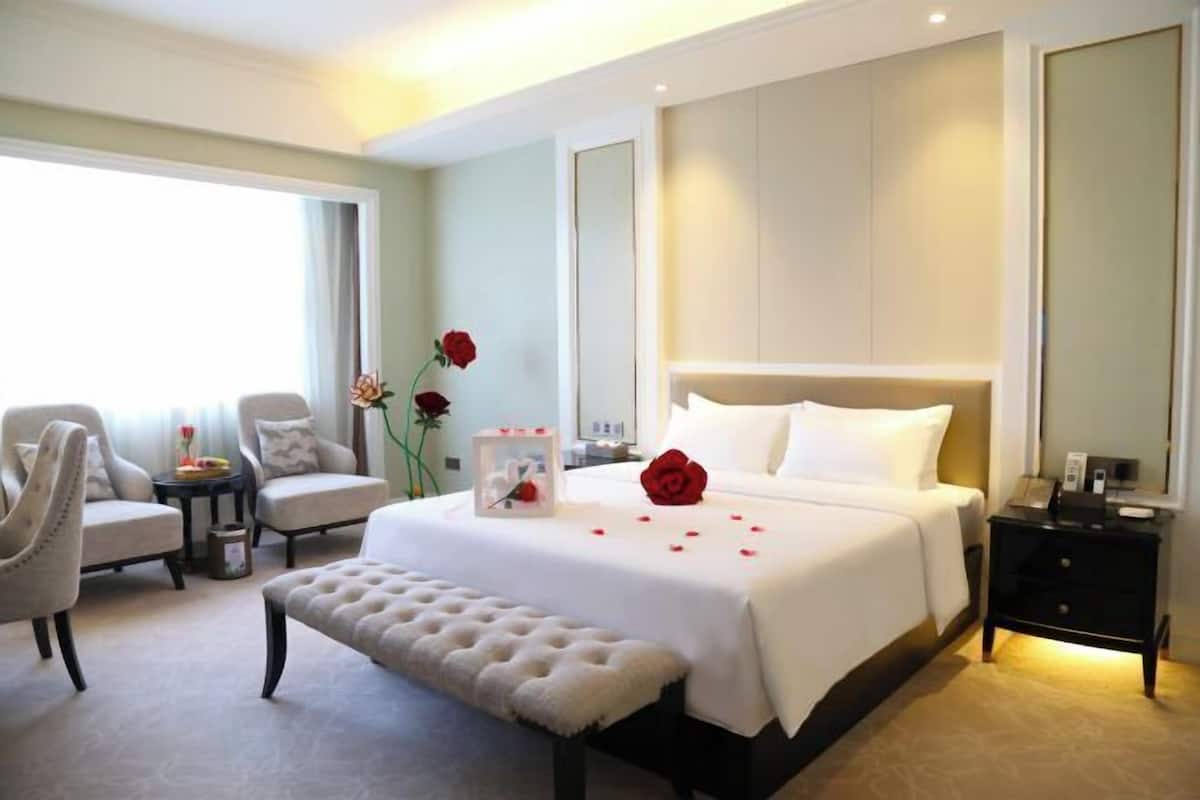 Habitación de hotel con una cama grande, dos sillones, una mesita, un banco y una mesita de noche.