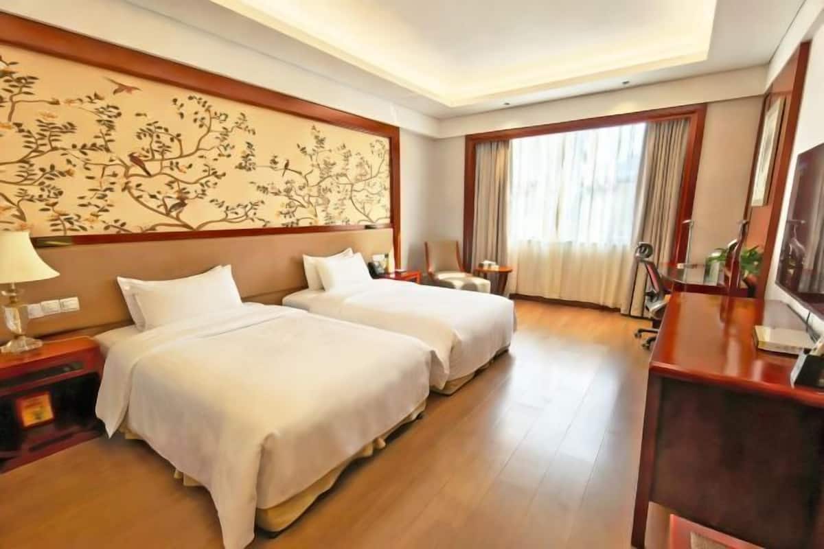 Habitación de hotel con dos camas, un escritorio, una silla, un televisor y un adorno en la pared.