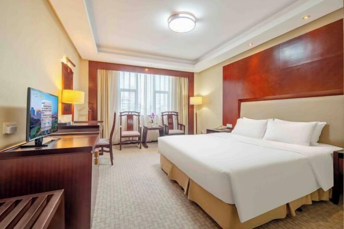 Una habitación de hotel con cama, escritorio, sillas, televisión y ventana.