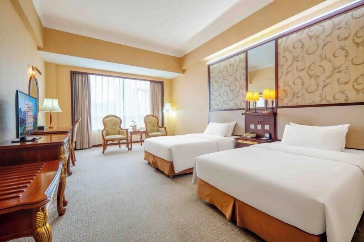 Habitación de hotel con dos camas, un escritorio, una silla, un televisor y un ventanal amplio.
