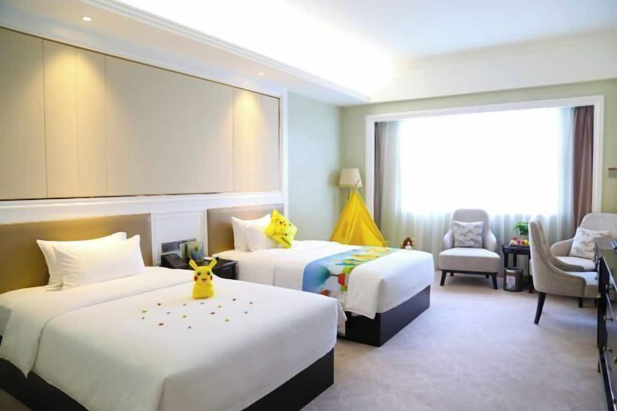 Habitación de hotel con dos camas, un escritorio, una silla y un ventanal grande.
