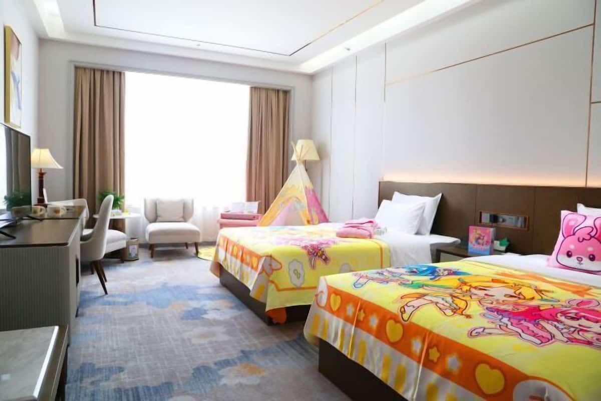 Habitación de hotel con dos camas, un escritorio, una silla, una lámpara y una ventana con cortinas.