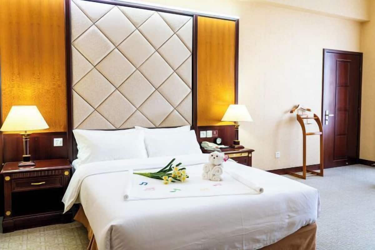 Una habitación de hotel con una cama grande, dos mesitas de noche, un cabecero de madera y un pequeño escritorio con una lámpara.