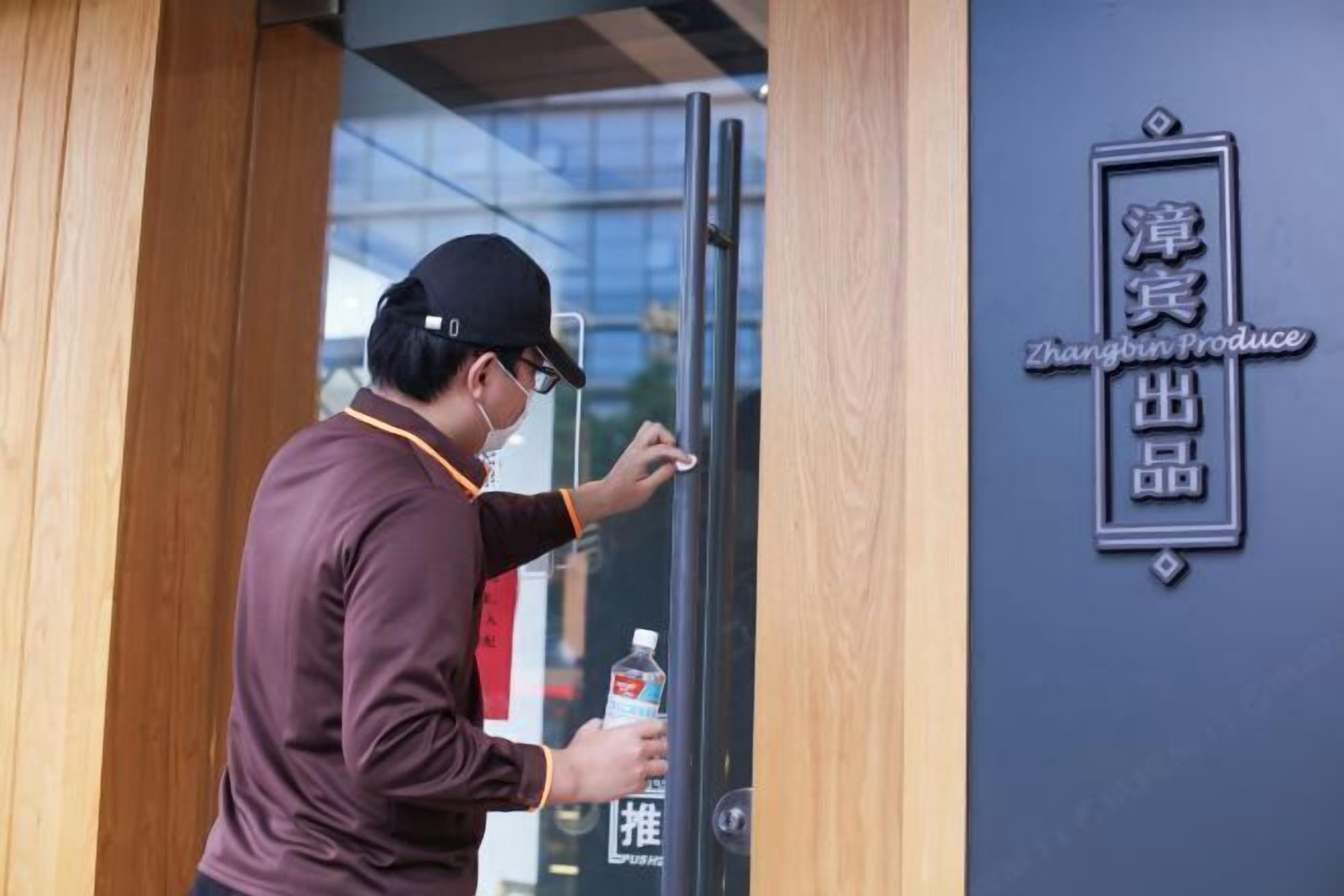 A person opening a glass door to a building with a sign that reads "Zhangbin Produce".