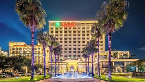 Un hotel con una fontana centrale, circondato da palme e un ingresso ben illuminato.