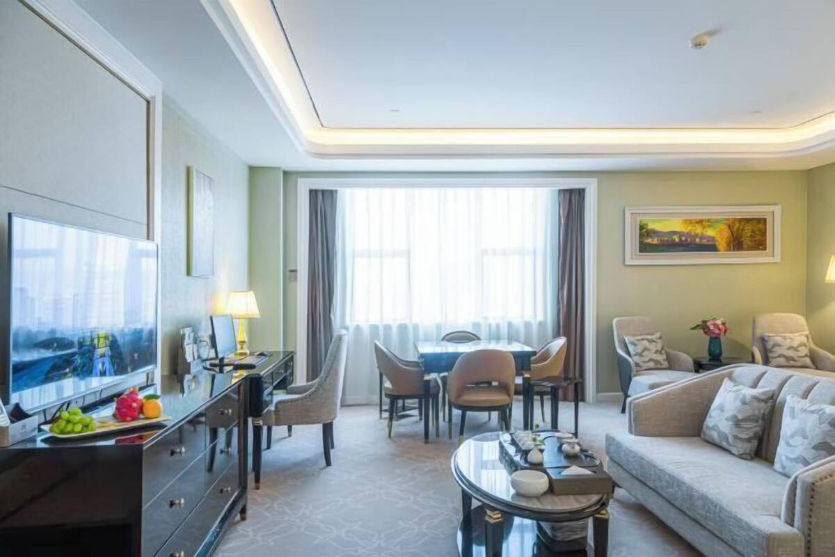 Una habitación de hotel con televisión, una mesa de comedor, sillas, un sofá y un cuadro en la pared.