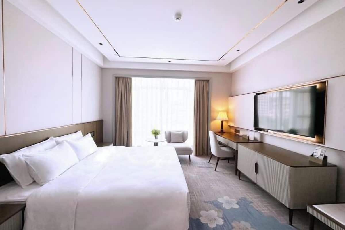 Habitación de hotel con una cama grande, un escritorio con televisor de pantalla plana, una silla y una mesita.