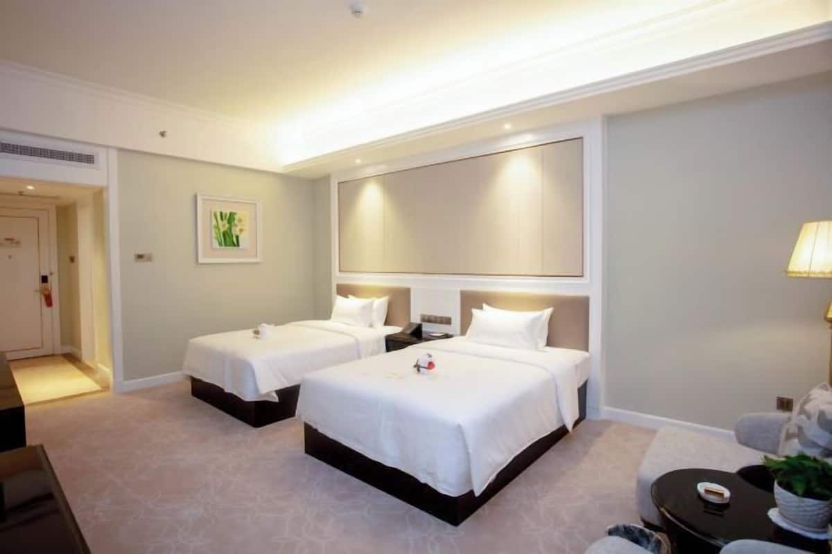 Una habitación de hotel con dos camas, una mesita de noche, una lámpara y un pequeño rincón de descanso.