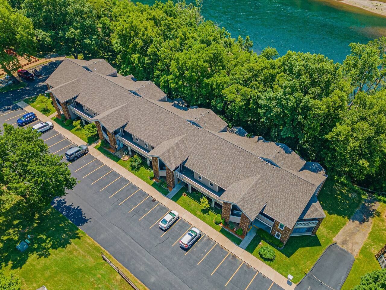 An aerial view of a multi-story building with a parking lot, surrounded by trees and a body of water.