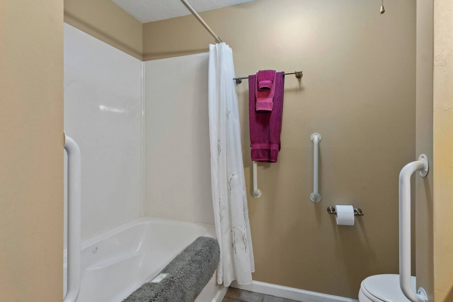 Ein Badezimmer mit Dusche, Toilette und Haltegriffen.