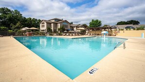 Une piscine rectangulaire dont la profondeur est indiquée à 4 pieds, entourée de chaises longues et de parasols, avec une grande maison en arrière-plan.