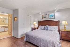 Une chambre à coucher avec un grand lit, deux tables de chevet avec des lampes, un miroir avec éclairage intégré et deux tableaux encadrés accrochés au mur.