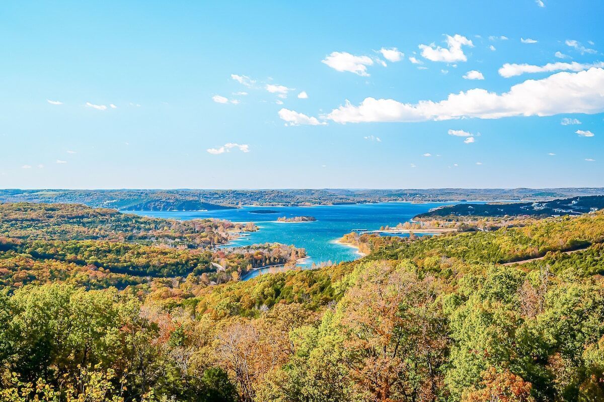 Une vue panoramique d’un paysage côtier, avec une vaste étendue d’eau, entourée de forêts denses et de collines.