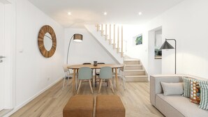 A modern living room with a sofa, ottomans, a dining table with chairs, a staircase, and a large mirror on the wall. - Surf & Chill Peniche Villa (Peniche)