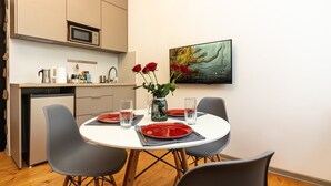 A dining area with a white table, grey chairs, and red plates. There is a microwave above the counter, a sink, and a cabinet with kitchen items. A vase with red roses is on the table. - City Hall apartment in 19th century house, heart of old town
 (Minsk)