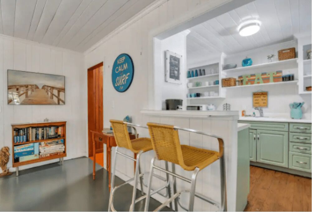 A kitchen with a bar area, a bookshelf, and a 'KEEP CALM SURF' sign.