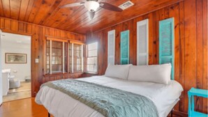 Une pièce en bois avec un lit, un ventilateur de plafond et des volets aux fenêtres.