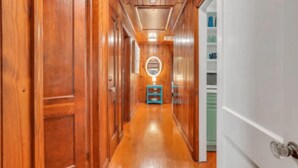 Un couloir en bois, orné d’un miroir rond au mur, mène à une pièce dont la porte est verte.