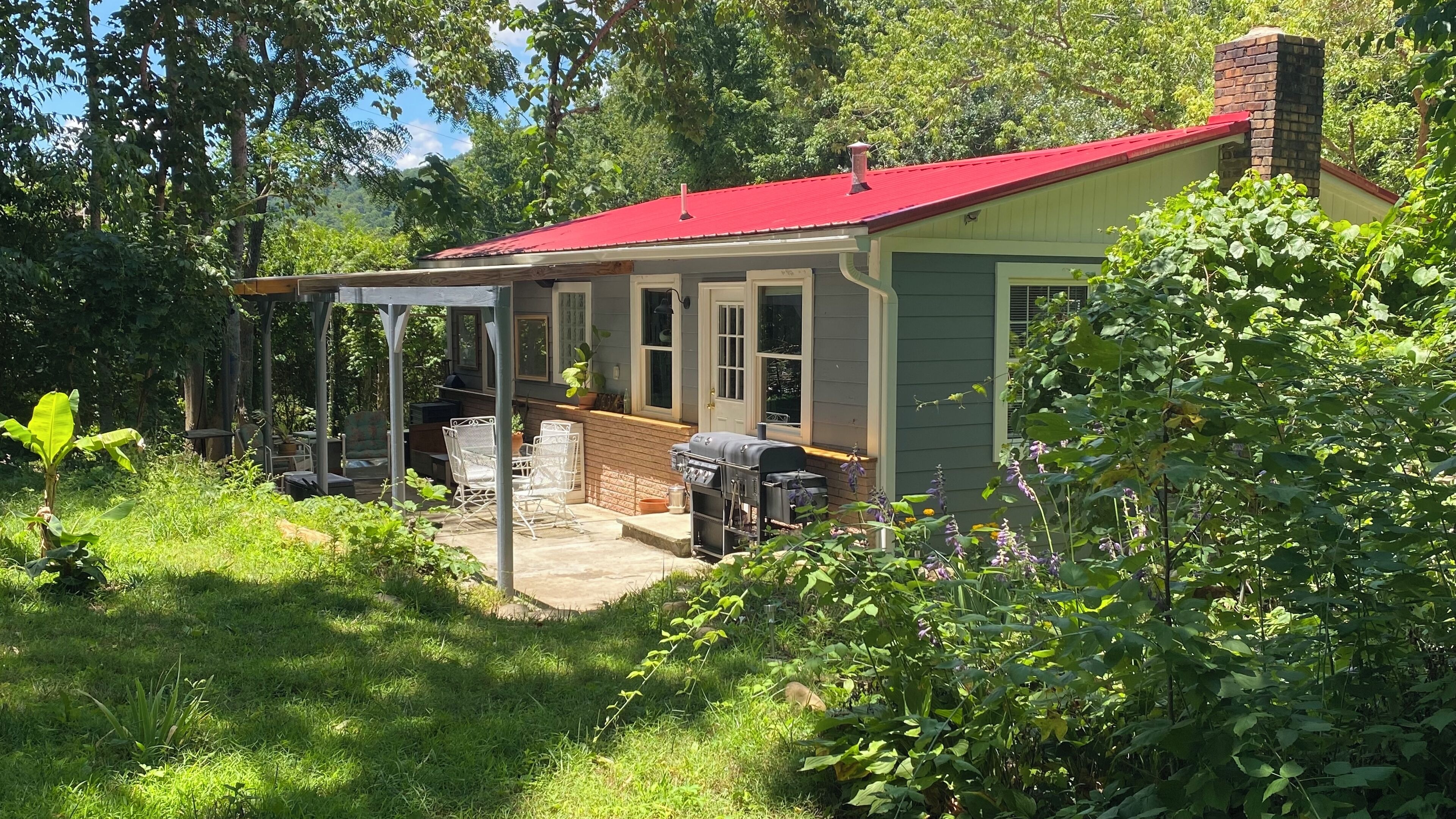 Ein Haus mit rotem Dach, einer überdachten Terrasse und einem Grill.