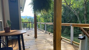 A wooden deck with a table and chairs, surrounded by a railing and greenery. - 3 Miles to Asheville! Sunfilled Cabin with Wi/Fi (Asheville)