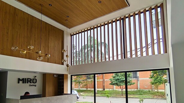 A modern interior with a reception desk labeled "MIRÓ Living," a large window with a view of the street, and a seating area with a sofa. - Cali, Colombia. Loft en zona exclusiva Miro Living 809 (Cali)