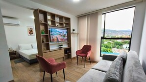 A modern living room with a flat-screen TV, a grey sofa, two red chairs, and a wooden entertainment unit. - Cali, Colombia. Loft en zona exclusiva Miro Living 809 (Cali)