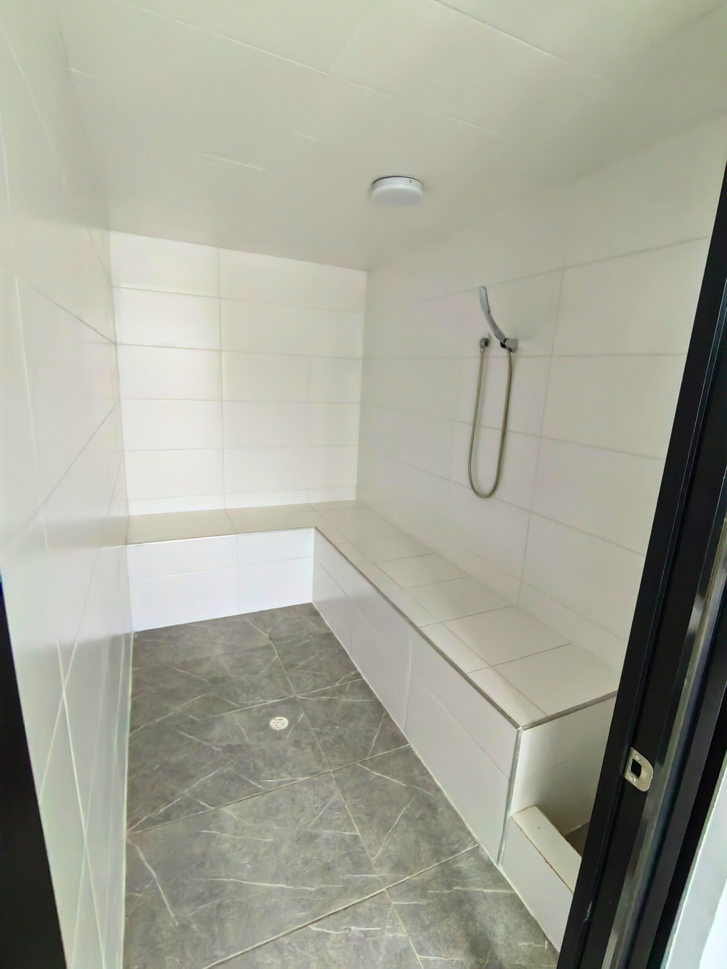 A small, tiled bathroom with a shower, a bench, and a tiled floor.